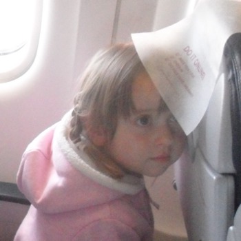 Ульяна прячется от фотоаппарата в самолёте под салфеткой впереди стоящего кресла.